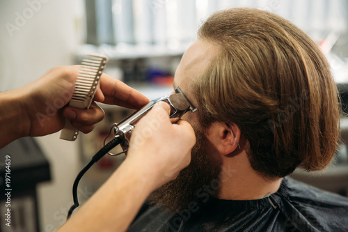 Bearded man having a haircut with a hair clippers. Closeup view with shallow depth of field