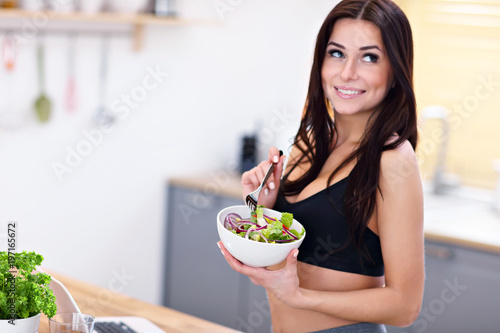 Fit smiling young woman with salad in modern kitchen