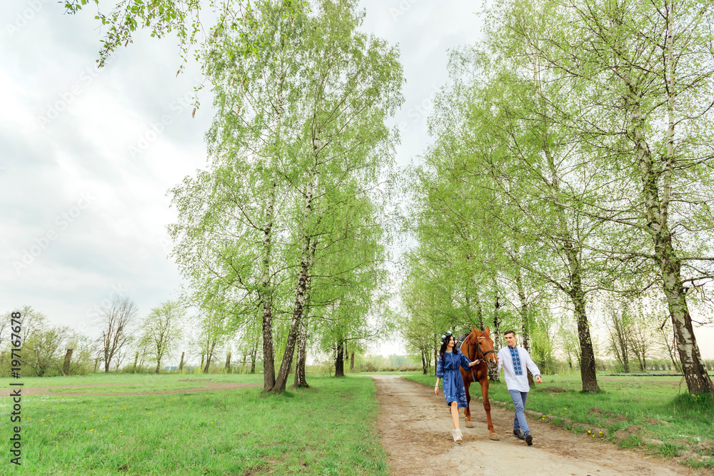 a guy and his girlfriend in festive clothes walk around the village and keep a horse behind the bridle a guy and his girlfriend in festive clothes walk around the village and keep a horse behind the bridle
