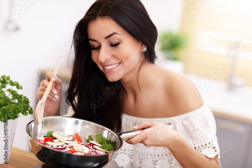 Young woman preparing fried vegetables in kitchen