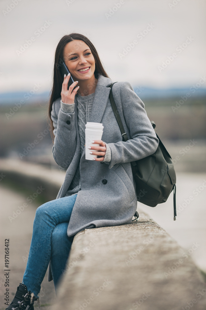 Young woman is talking on phone and drinking coffee after work.