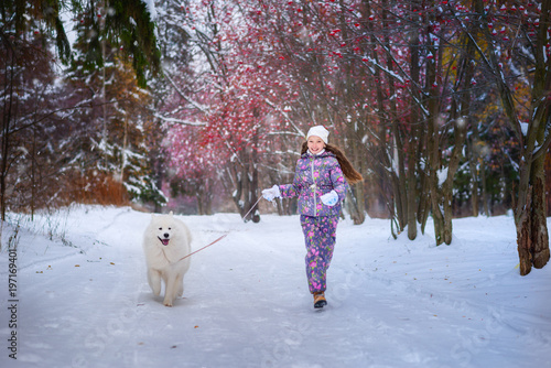 Девочка с собакой породы самоед на прогулке в зимнем парке