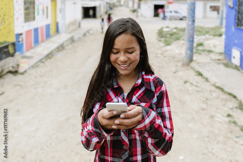 Photography Portrait of cute latino girl using the mobile in shanty town.