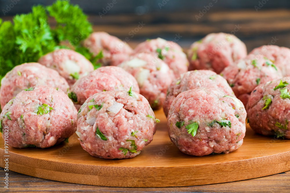 © Magrig - Raw meatballs on wooden cutting board and fresh parsley, close-up