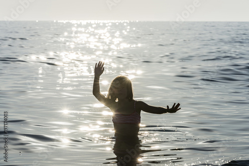 Little girl bathing in the sea surrounded by sunbeam reflections