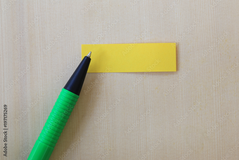 Green pen pointing to empty yellow paper note on wooden floor background. Green pen pointing to empty yellow paper note on wooden floor background.