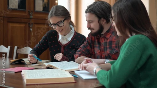 Wallpaper Mural Happy friends discussing data as working on project in the library, pretty intellectual girls pointing at the text, bearded young man turning book pages, concept of teamwork Torontodigital.ca