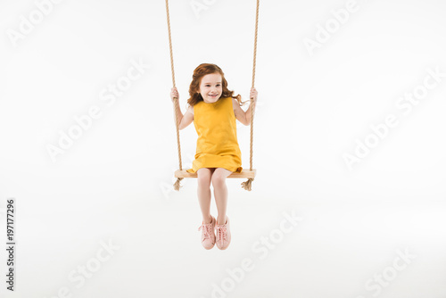 Fotografi Little stylish child in dress riding on swing isolated on white