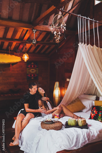 Young couple in love having breakfast in bed in traditional indian wooden house in hippie style