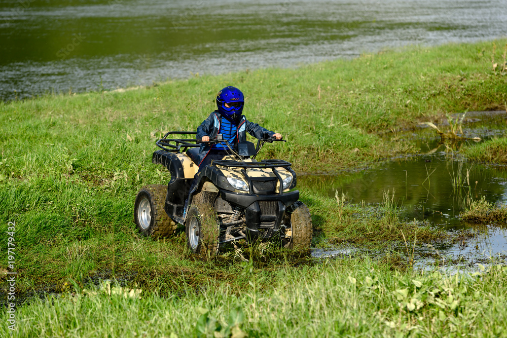 The boy is traveling on an ATV. The boy is traveling on an ATV.