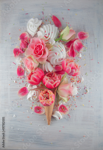 Flatlay waffle sweet ice cream cone with pink tulips and roses blossom flowers over white wood background, top view. Spring or summer mood concept.
