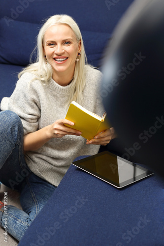 Relaks z książką. Piękna blondynka czyta książkę siedząc w domu