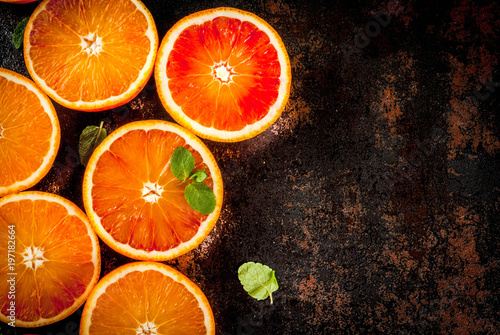 Fresh raw blood oranges, halves, with mint, on dark rusty background copy space top view