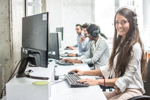 Beautiful smiling woman costumer support worker with headset using computer in call center.