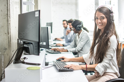 Beautiful smiling woman costumer support worker with headset using computer in call center. photo