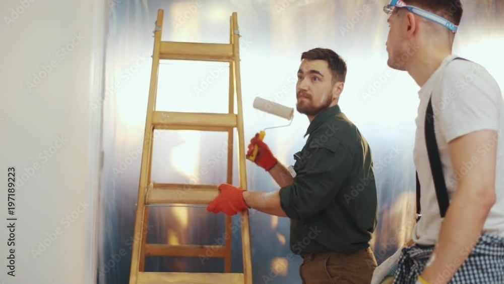 The foreman points at the wall, gives an advice to his co-worker to repaint it again. Process of refreshment, high quality, skilled workmen. Slow motion, camera stabilizer shot The foreman points at the wall, gives an advice to his co-worker to repaint it again. Process of refreshment, high quality, skilled workmen. Slow motion, camera stabilizer shot