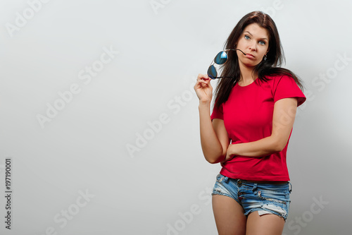 A young, beautiful girl is holding sunglasses in her hand. Isolated on a light background. Different human emotions, feelings of facial expression, attitude, perception, body language, reaction.