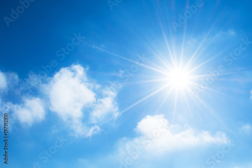 The sun with bright rays in the blue sky with white light clouds.