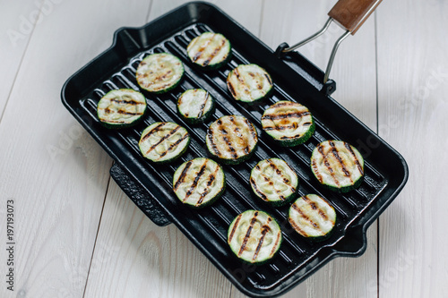 Zucchini grilled on a black pan. Light wooden background.