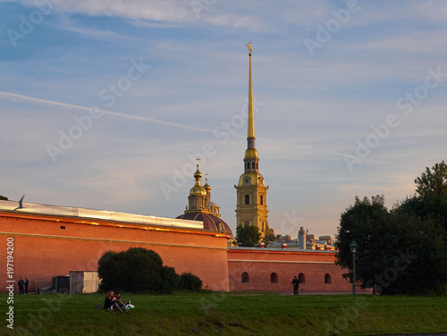 Peter and Paul Fortress at sunset. Saint Petersburg, Russia. Tourists resting on a riverbank photo