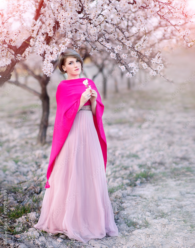 Young woman in the gardens of blossoming almonds in a beautiful long dress Young woman in the gardens of blossoming almonds in a beautiful long dress