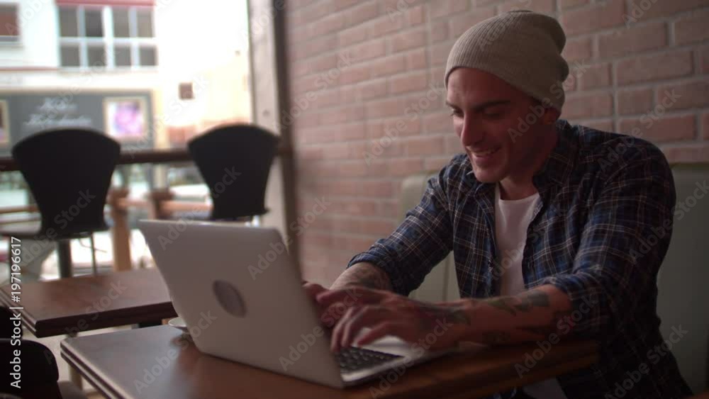 Young hipster chatting online using laptop, laughing at coffee shop Young hipster chatting online using laptop, laughing at coffee shop