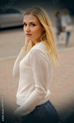 Pretty young woman in white sweater posing in a street