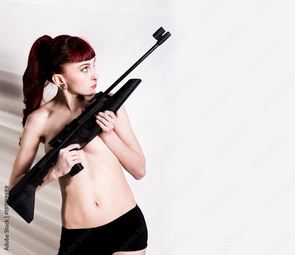 Beautiful sexy redhead holding pneumatic weapon on a light background. free space for your text