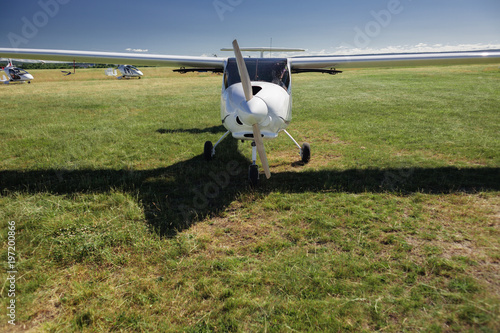 A small white light-engine aircraft with a propeller stands in the middle of a field with green grass on a summer clear sunny day. photo