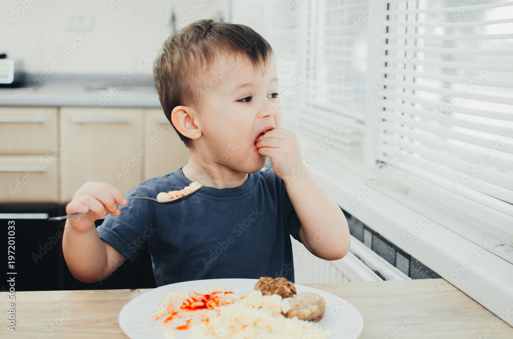 little baby boy in the kitchen eating pasta with cutlets, very tasty little baby boy in the kitchen eating pasta with cutlets, very tasty