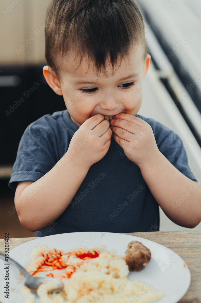 little baby boy in the kitchen eating pasta with cutlets, very tasty little baby boy in the kitchen eating pasta with cutlets, very tasty