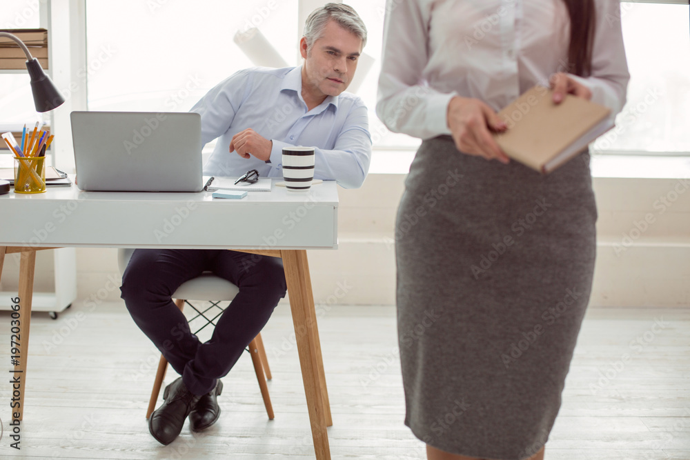 At the office. Smart nice adult man sitting at the table and pretending to  work while looking at his female colleague Stock Photo | Adobe Stock