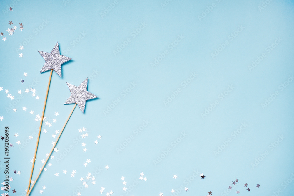 Two silver party magic wands and scattered sequins on a blue background. Copy space.