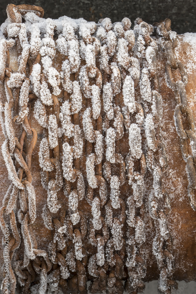 Obraz premium The frozen rusty chain is wound on a log, to raise a bucket of water from an old well, a frosty day.