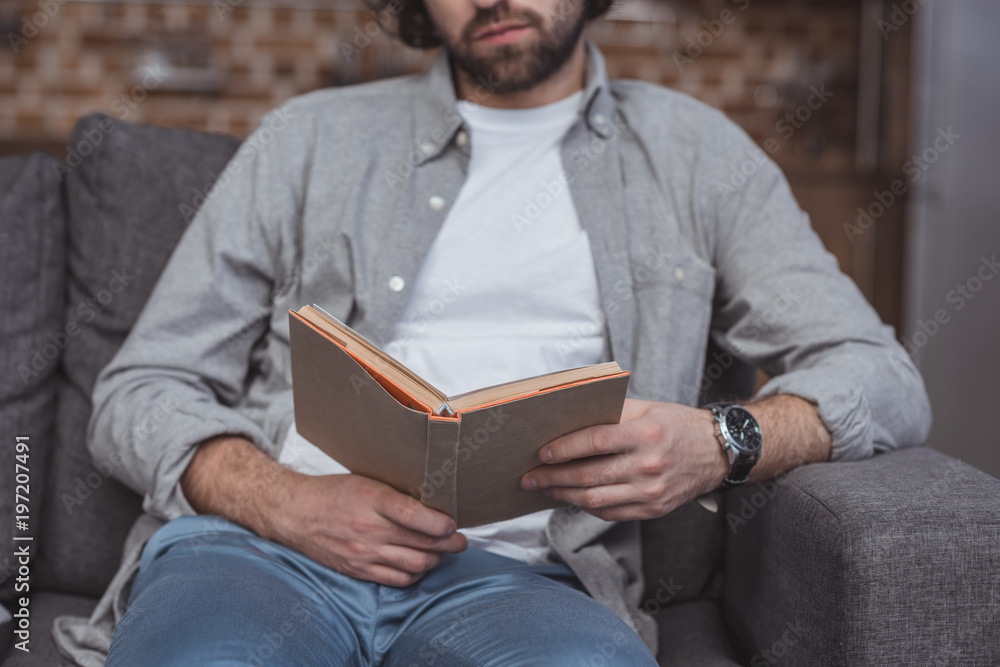 cropped image of man reading book on sofa at home