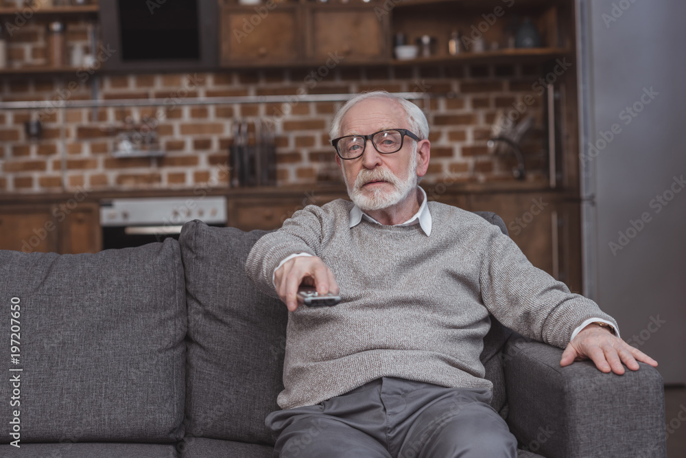 Fototapeta premium handsome grey hair man changing tv channels with remote control at home
