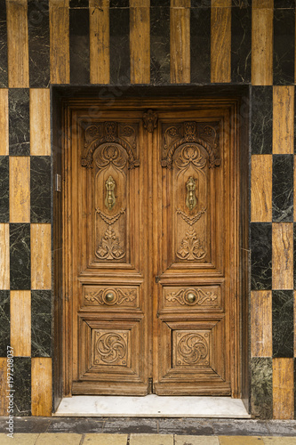 Puerta antigua de madera en fachada de mármol negro y marrón. © Lola Fdez. Nogales