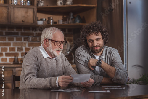 adult son and senior father looking at old photos at home