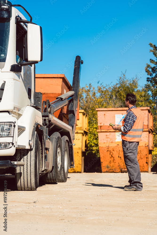 Fototapeta premium Bauarbeiter auf Baustelle lädt Bauschuttcontainer ab mit Fernbedienung 