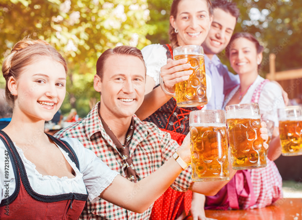 Im Biergarten - Freunde in Lederhosen und Dirndl trinken eine frische Maß Bier Im Biergarten - Freunde in Lederhosen und Dirndl trinken eine frische Maß Bier