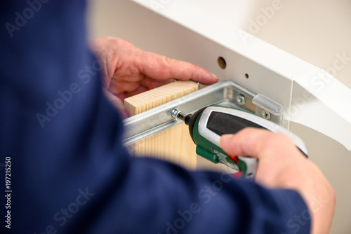 Close up on hands with cordless screwdriver assembling furniture