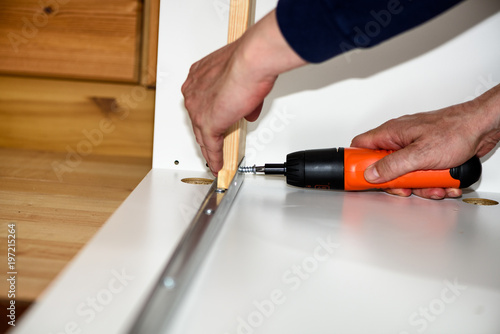 Close up on hands with cordless screwdriver assembling furniture