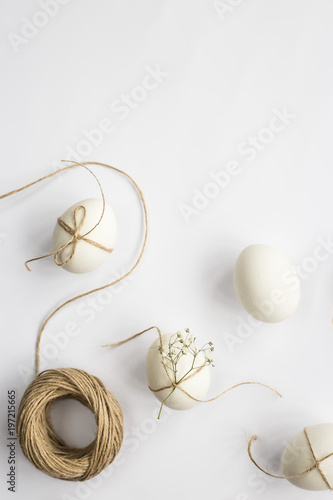 Easter eggs are minimalistically decorated with twine and gypsophila flowers. On a white background with a brown rope. Top view, flat lay. Copyspace