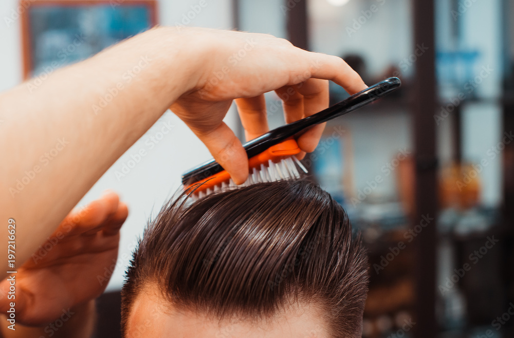 Fototapeta premium Master cuts hair and beard of men in the barbershop, hairdresser makes hairstyle for a young man