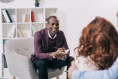 Smiling african american psychiatrist talking to young couple photo
