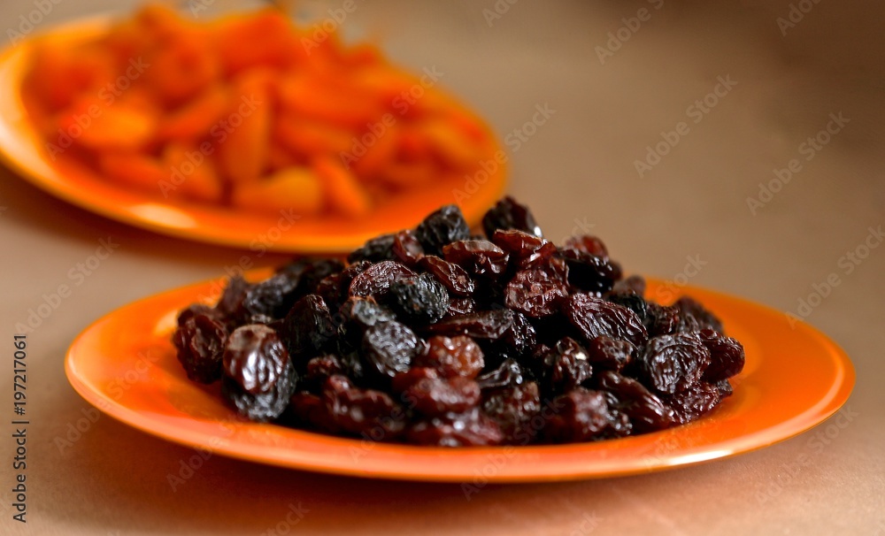 dry black grapes - raisin, red dried apricots on a red glass plate on a table dry black grapes - raisin, red dried apricots on a red glass plate on a table