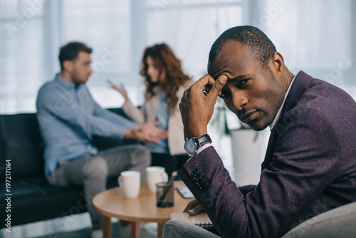 Tired african american psychiatrist and arguing couple sitting on sofa