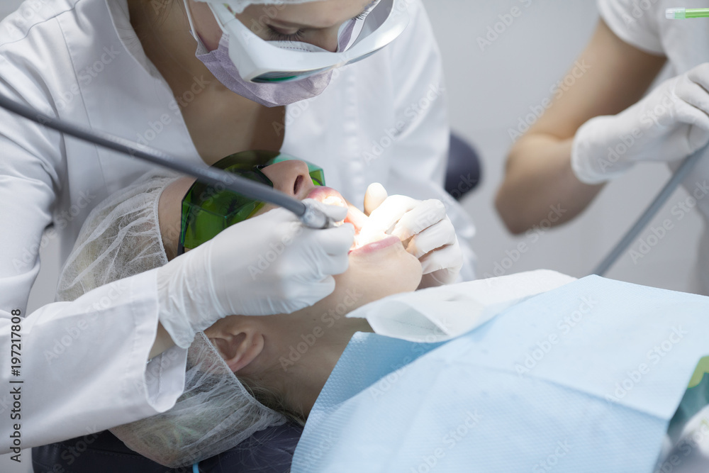 Naklejka premium Doctor dentist treats teeth of a beautiful young girl patient. The girl on reception at the dentist. Doctor dentist treats tooth.