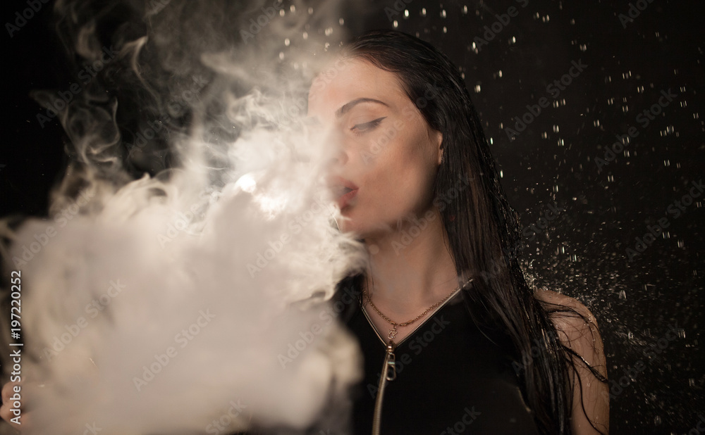 Young beautiful woman vaping e-cigarette in rain. Water flowing on woman face.