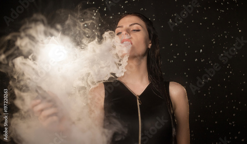 Young beautiful woman vaping e-cigarette in rain. Water flowing on woman face.